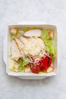 Sezar salatası paket olarak paket olarak servis edilecek. Tarafsız gri arka planda.