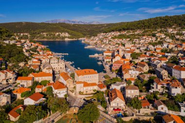Hırvatistan 'ın Brac adasının Pucisca kasabasındaki derin körfezdeki kırmızı çatılar ve beyaz taş evler. Ağustos 2020 'de havadan panoramik dron görüntüsü
