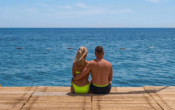 Pärchen sitzen am Holzsteg, umarmen sich und blicken auf das türkisfarbene Wasser des Mittelmeeres in Tekirova, Kemer, Türkei. Mai 2021 — Stockfoto