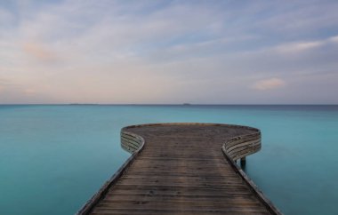 Tahta köprü ya da güneşli bir günde açık mavi okyanus ve gökyüzü olan tropikal beyaz kumsaldaki iskele. Okyanusa doğru tahta yürüyüş ve turkuaz su. Fotokopi alanı olan yaz tatilleri. Kesişen yollar