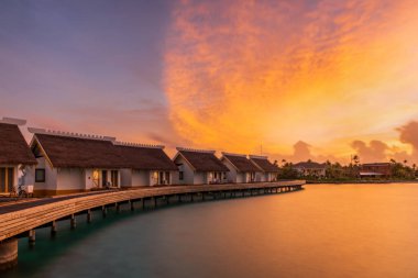 Su bungalovlarının üzerinde gün batımında inanılmaz yeşil bir göle adım atıyorlar. Maldivler Kavşağı, Temmuz 2021