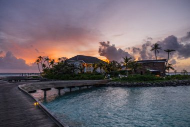 Su bungalovlarının üzerinde gün batımında inanılmaz yeşil bir göle adım atıyorlar. Maldivler Kavşağı, Temmuz 2021