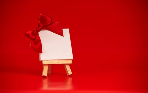 wooden easel with blank canvas on christmas red background