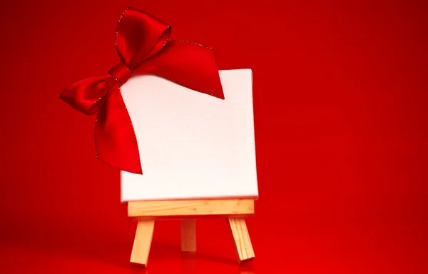 wooden easel with blank canvas on christmas red background