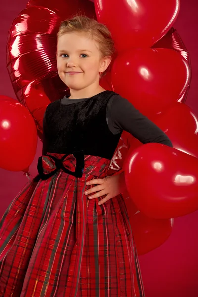 Lächelndes kleines Mädchen mit einem Bündel roter herzförmiger Luftballons — Stockfoto