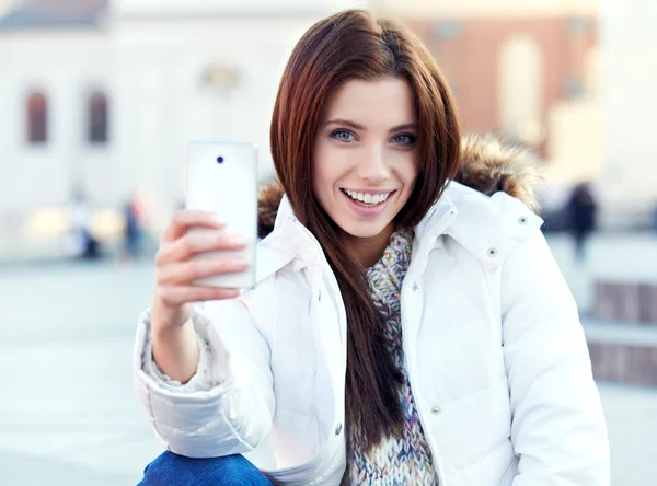 Una mujer joven y bonita tomando una foto en la ciudad. Chica sonriente. Winte. —  Fotos de Stock