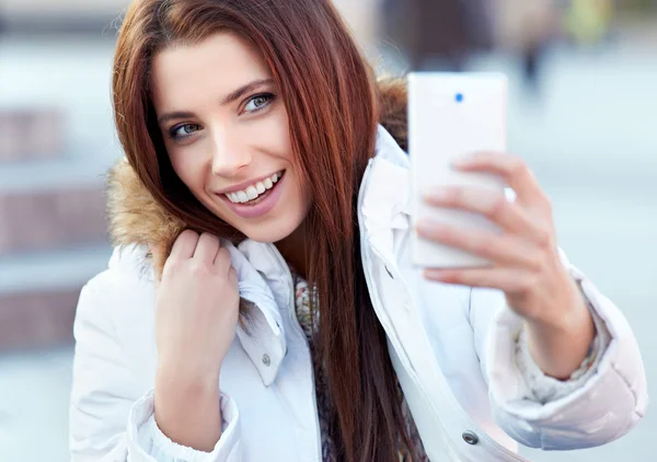 Una mujer joven y bonita tomando una foto en la ciudad. Chica sonriente. Winte. —  Fotos de Stock