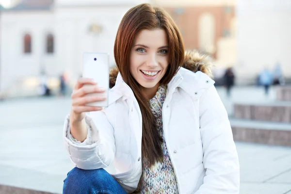 Una mujer joven y bonita tomando una foto en la ciudad. Chica sonriente. Winte. —  Fotos de Stock