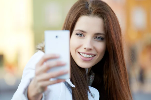 Una mujer joven y bonita tomando una foto en la ciudad. Chica sonriente. Winte. —  Fotos de Stock