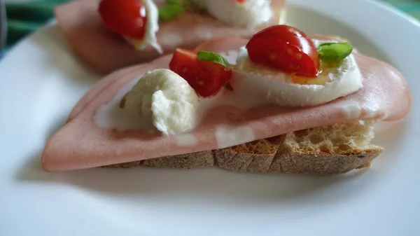 Um sanduíche aberto com pão caseiro, mortadela, mussarela, tomate cereja, manjericão — Fotografia de Stock