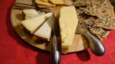 Ahşap bir tabakta servis edilen karışık inek peynirleri ve toptan ekmek dilimleri.