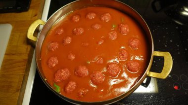 Ev yapımı köfteler domates soslu bir tavada yavaşça pişiyor.