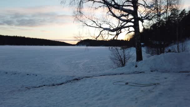 人々は北欧の凍った湖で日没時に静かに散歩します — ストック動画