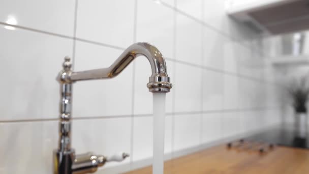 Water flowing out of stainless steel tap. Dish rack holds dishes against wooden countertop, white wall tiles, sink and faucet. Budget lightweight dish drainer with drain board at scandinavian kitchen — Stock Video