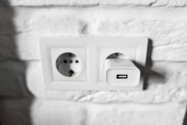 Unplugging idle appliances saves electricity. Idle phone chargers or power adapters. Vampire power, standby power. Plug-in adapter into european wall outlet. USB plug insert into electric wall socket — стоковое фото