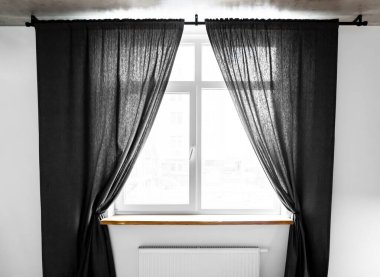 Two separate linen curtain panels with tieback in classic and contemporary bedroom. Panel pair cotton curtains tied back at the modern window. Semi-sheer black floor length curtains on the metal rod. clipart
