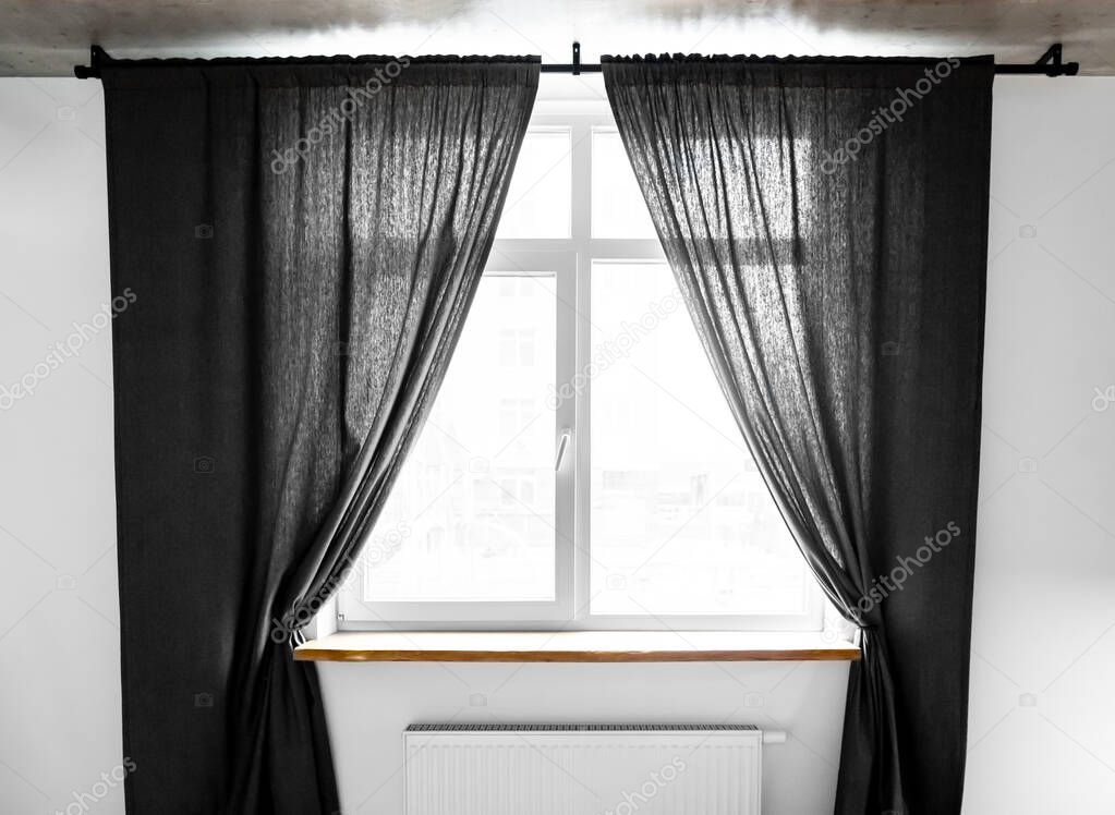 Two separate linen curtain panels with tieback in classic and contemporary bedroom. Panel pair cotton curtains tied back at the modern window. Semi-sheer black floor length curtains on the metal rod.
