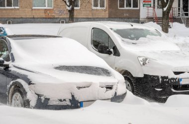 Kar fırtınasından sonra şehir caddesi. Kar ve buzun altında sıkışmış arabalar. Gömülü araç yolda kar yığınında. Yoğun kar yağışından sonra kışın otopark. Temizlenmemiş yollar. Rekor miktarda kar yağıyor..