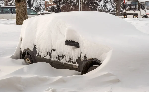 Stadtstraße nach Schneesturm. Autos stecken unter Schnee und Eis fest. Fahrzeug bei Schneeverwehungen auf der Straße verschüttet Parkplätze im Winter nach starkem Schneefall. Ungereinigte Straßen. Rekordschneemengen. Stockbild