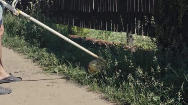 Amatér řeže trávu benzínovým kartáčovým nebo travním nůžkovým strojem se třemi ocelovými noži ve tvaru hvězdy a s deflektorem trávy. Zahradní nebo zemědělský nástroj používaný k úpravě plevele. Ruční nůžky na kartáče — Stock video