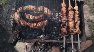 Barbekü et ve sosis ya da arka bahçede ızgarada ızgara sosis. Şiş kebap hazırlayan ya da kömürün üstüne şiş kebap yapan adam. Dışarıdaki metal şişte ızgara et. Mangal partisi ya da piknik yemeği. Yakın çekim.