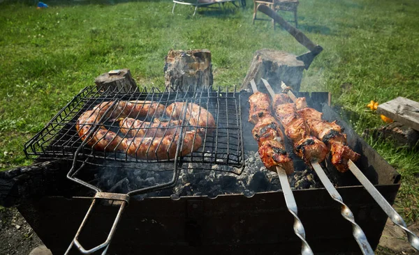 Carne de barbacoa y salchichas o salchichas en una parrilla en el patio trasero. Hombre preparando shashlik o shish kebab sobre carbón vegetal. Carne a la parrilla en pincho de metal al aire libre. Fiesta de barbacoa o picnic. Primer plano. —  Fotos de Stock