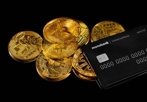 Lutsk, Ukraine - 1. Mai 2021: Goldmünze mit Bitcoin-Logo und Kreditkarte der Monobank. Kryptowährung BTC und Bitcoin Belohnungskarte von Universal Bank. Digitales elektronisches Geld oder E-Cash-Zahlung lizenzfreie Stockfotos