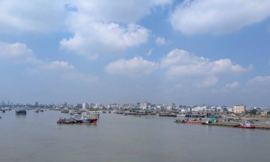 Gün içinde parçalı bulutlu gökyüzünün altında kayıklar ve şehir silueti olan nehir manzarası