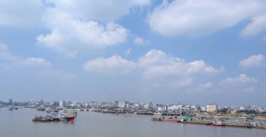 Gün boyunca deniz kenti manzarası sakin. Tekneler, binalar ve bulutlu açık bir gökyüzü sergileniyor.