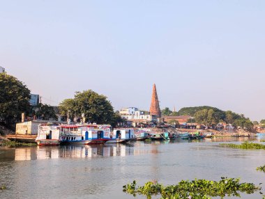 Nehir kenarındaki bir kasabada gün ışığında nehir kıyısı boyunca dizilmiş tekneler, arka planda ağaçlar ve binalar vardı.
