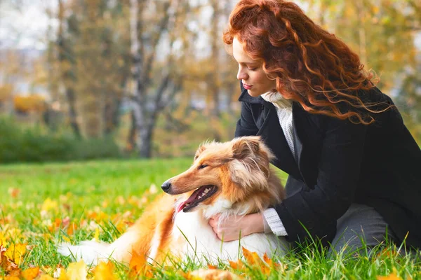 Милая женщина с рыжими волосами гладит и обнимает свою колли-собаку. Женщина в осеннем парке на открытом воздухе, домашнее животное. — стоковое фото