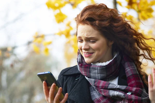 Elinde cep telefonu olan öfkeli, şaşırmış bir kadın. Huysuz kadın dışarıda akıllı telefon tutuyor.