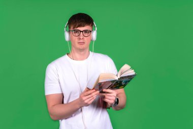 Dalgın, kulaklıklı, ciddi bir adam, kitap okuyor. Erkek, erkek öğrenci sesli kitap dinliyor. Yeşil izole arkaplanda