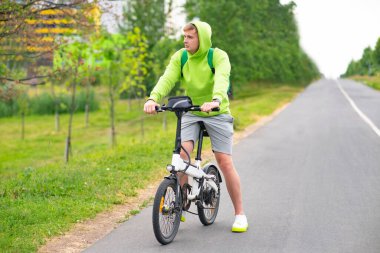 Elektirikli bisiklet süren, yaz parkında bisiklet süren üzgün genç adam. Aktif erkek yaşam tarzı, spor