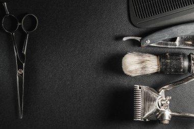 Siyah bir yüzeyde eski berber aletleri vardır.İki adet eski el yapımı saç makası, tarak, jilet, tıraş fırçası, kuaför makası. siyah monokrom. Yakın plan. Berber dükkanı geçmişi. farklı gölgeler. Yatay oryantasyon. Üst manzara, düz yatış. Boşluğu kopyala