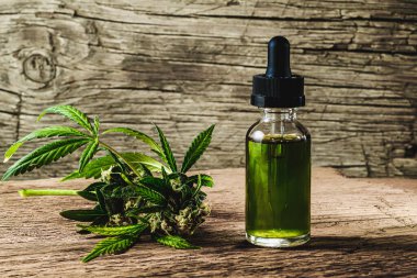 Bitkisel organik ilaç içeren cam şişe CBD konsantrasyonu, bitkisel ve ekolojik kenevir bitkisinin bitkisel cbd yağını bir kavanozdan ve ahşap zeminde tıbbi kenevir tomurcuğundan enjekte eden damlacık. Yatay yönelim.