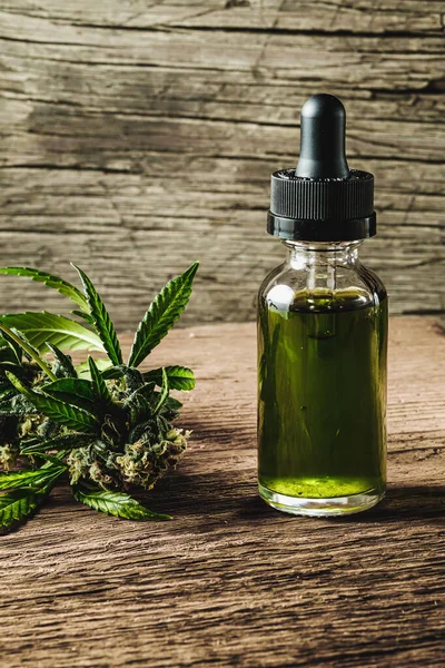 Glass bottle with herbal organic medicine CBD concentrate, droplet dosing a biological and ecological hemp plant herbal pharmaceutical cbd oil from a jar and medical cannabis bud on wooden background. Vertical orientation.
