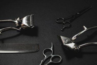 Siyah bir yüzeyde eski berber aletleri vardır. Klasik manuel saç makası, tarak, kuaför makası. siyah monokrom. Siyah arka plan. farklı gölgeler. yatay.