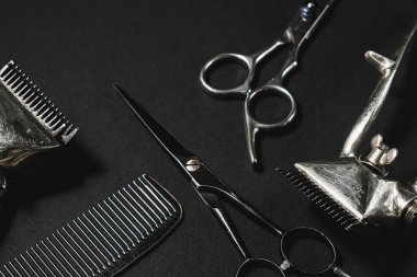 Siyah bir yüzeyde eski berber aletleri vardır. İki klasik manuel saç makası, tarak, kuaför makası. siyah monokrom. farklı gölgeler. Üst manzara, düz uzanma.