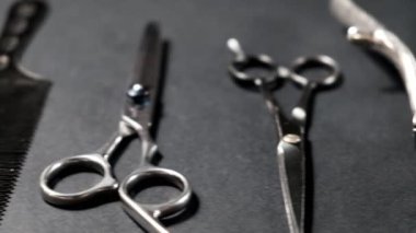 Siyah bir yüzeyde eski berber aletleri vardır. Klasik manuel saç makası, tarak, jilet, kuaför makası. siyah monokrom. Yakın plan. Berber dükkanı geçmişi. farklı gölgeler. kaydırıcı hareketi.