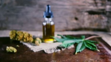 Bir şişe esrar konsantresi CBD, kurumuş marihuana tomurcukları ve tahta bir çuval kumaş arka planında kenevir yaprağının yanında duruyor. 4k