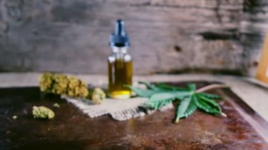 Bir şişe esrar konsantresi CBD, kurumuş marihuana tomurcukları ve tahta bir çuval kumaş arka planında kenevir yaprağının yanında duruyor. 4k