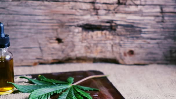 在干枯的大麻芽旁边 有一小瓶大麻精Cbd 在木制麻布背景上有一片大麻叶 — 图库视频影像