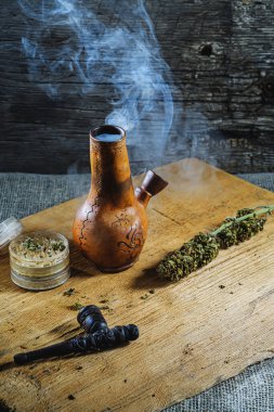 Eski kahverengi buhar bongu ve açık kenevir öğütücüsü ile doğranmış marihuana otu ve tıbbi kenevir tomurcuğu ahşap tüy ve çuval bezi ile duman içinde. Dikey yönelim