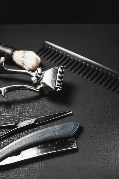 On a black surface are old barber tools. Vintage manual hair clipper comb razor shaving brush shaving brush hairdressing scissors. black monochrome. vertical orientation