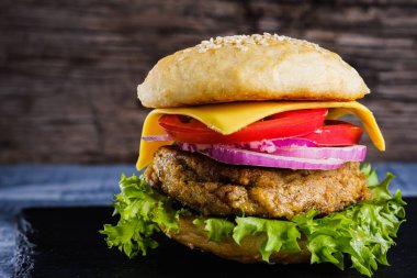 Taze lezzetli ev yapımı vejetaryen burger, sade ahşap arka planda, doğal bir levhada yatar. Marul, peynir, soğan ve domatesli lezzetli hamburger. Karabuğday ve mercimek pirzolası. yatay orinasyon