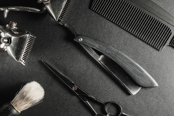 Op een zwart oppervlak staan oude kappersgereedschappen. twee vintage handbediende tondeuse, kam, scheermes, kappersschaar. zwart monochroom. Een close-up. Barbershop achtergrond. contrastschaduwen. horizontaal Stockfoto