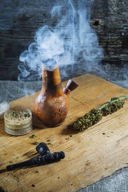 Eski kahverengi buhar bongu ve açık kenevir öğütücü ile doğranmış marihuana esrarı ve dumanlı tıbbi kenevir odunu ve çuval bezi. Yatay