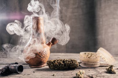 Ahşap yüzeyde tıbbi marihuanayla birlikte tüttüren eski bir balçık nargilesi var.