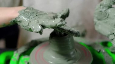 Yedi yaşında, kille kirlenmiş bir çocuk çömlekçi çarkında kilden bir ürün yapmaya konsantre oluyor. Yakın plan. Yatay.